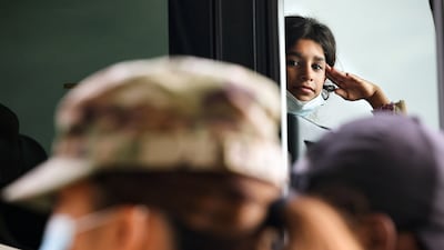 A young Afghan refugee salutes a member of the US Army as she waits on a bus after arriving at Dulles International Airport in Dulles, Virginia. Reuters