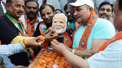Indian supporters offer sweets to another wearing a mask of the newly sworn-in Indian Prime Minister Narendra Modi. AFP