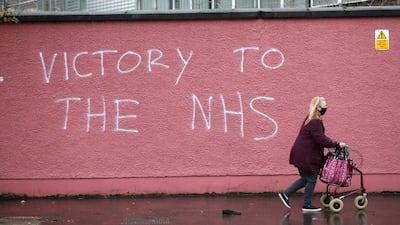A woman walks past graffiti with the words Victory to the NHS on a wall at the Royal Victoria Hospital in West Belfast, Northern Ireland. AP Photo
