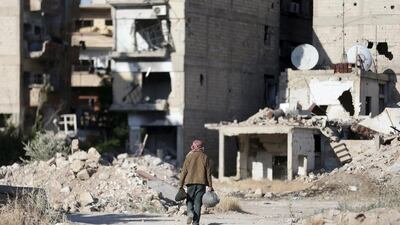 A man carries his belongings as he walks past damaged buildings along a street in Jobar, a suburb of Damascus. (REUTERS/Bassam Khabieh)