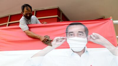 An Indonesian worker wears a face mask as he cleans a coronavirus safety awareness campaign banner featuring Indonesian President Joko Widodo, in Jakarta. EPA