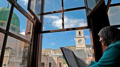An elderly Palestinian woman reads the Quran at her window overlooking the Manara clock tower and Al Nasr Mosque in the old town of the West Bank city of Nablus. AFP