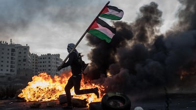 A Palestinian protester runs past a burning barricade carrying a Palestinian flag during clashes with Israeli border guards near an Israeli checkpoint. Chris McGrath/Getty Images