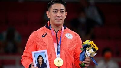 Japan's Ryo Kiyuna poses with his men's kata gold medal and holds a portrait of his late mother on the podium at a ceremony in the karate competition.