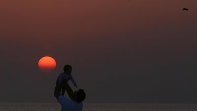 A man tosses a baby against the red sunrise as birds fly past on the beach in Kuwait City on the last day of the Eid al-Fitr holiday. AFP