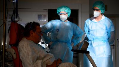A Swiss army soldier, right, wearing personal protective equipment helps hospital's physiotherapists to treat a Covid-19 patient in the intermediate care units of Geneva University Hospital. AP