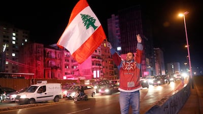 An anti-government protester flashes the victory sign and waves a Lebanese flag, as other protesters block a main road during ongoing protests against corruption and financial crisis, in Beirut, Lebanon. AP