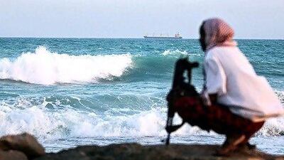 An armed Somali pirate keeps vigil on the coastline at Hobyo, northeastern Somalia, while a hijacked cargo ship is anchored just offshore. But after years of maritime lawlessness, victim nations are fighting back.
