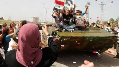 Syrian women shower army troops with rose petals and rice as youths holding up portraits of President Bashar al Assad ride on an army tank pulling out of the southern protest hub of Daraa today. This picture was taken on a government-sponsored tour.