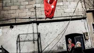 A man hangs a Turkish flag as two women stand in the doorway of their damaged house in Kilis a day after rockets hit the border town, leaving one dead. Yasin Akgul / AFP Photo