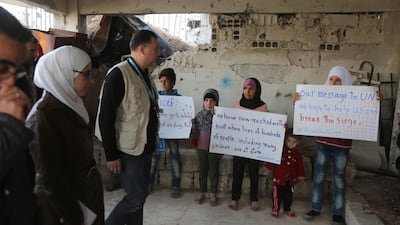 Syrian children hold messages pleading for help as members of an aid convoy enter a building during a humanitarian delivery in Al Nashabia town in the rebel-held Eastern Ghouta region outside Damascus on November 28, 2017. The Syrian conflict accounts for more than a third of the UN's projection for humanitarian assistance required in 2018. Amer Almohibany / AFP
