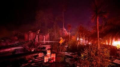 A firefighter hoses down hotspots left in a house destroyed by wildfire. EPA