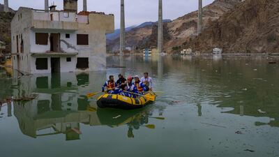 Volonteers from an animal rights NGO Haytap paddle a dinghy as they search for stray cats an dogs to rescue in the town of Yusufeli as it is gradually submerged by an artificial lake caused by a dam retaining the flow of the Coruh river (also referred to as Chorokhi), in Yusufeli, Artvin province, in northeastern Turkey, on April 4, 2022. - The Yusufeli Dam and its Hydroelectric Power Plant Project in the Eastern Black Sea Region has started to hold water, with the electricity production expected to start in May 2023. With a total water storage volume of approximately 2. 2 billion cubic meters, the double curvature concrete arch dam is Turkey’s highest with a height of 275 meters. (Photo by Yasin AKGUL / AFP)