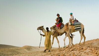 A man, a bedouin leading two camels with tourists, a mother and two children, Marsa Alam desert, Red Sea, Egypt. Getty Images