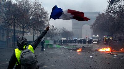 A protester wearing a yellow vest waves a French flag during clashes with riot police near the Arc de Triomphe in Paris. EPA
