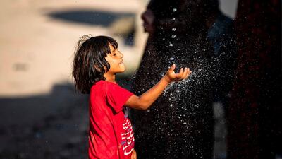 A Syrian boy plays with a stream of water, after humanitarian organisations delivered water to the area during a halt in water supply, in Syria's north-east city of Hasakah. AFP