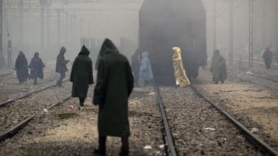 Migrants, one wearing a thermal blanket, walk on railway tracks at the northern Greek border station of Idomeni. Bad weather returned after a brief pause and conditions in the refugee camp on the Greek-Macedonian where about 14,000 people are stranded have further deteriorated. Vadim Ghirda / AP