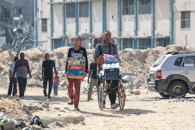 Palestinians walk with water and food aid through a heavly damaged residential district of the southern Gaza Strip city of Khan Yunis on July 5, 2024. AFP