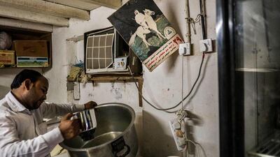 A merchant mixes cumin, black pepper and dried chili to make a blend called 'zir'. In the background hangs a poster celebrating the 29th year of Sheikh Zayed’s rule.