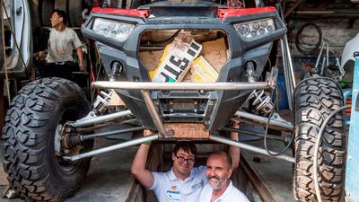 Jacques Barron and his son and co-driver Lucas Barron, 25, pose under their UTV at a mechanics workshop in Lima. AFP