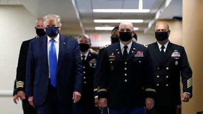 President Donald Trump, foreground left, wears a face mask as he walks with others down a hallway during a visit to Walter Reed National Military Medical Center in Bethesda, Md., Saturday, July 11, 2020. (AP Photo/Patrick Semansky)