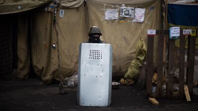 An anti-government protester wearing a balaclava and a military helmet stands behind an anti-riot police shield on Independence Square in Kiev. Martin Bureau / AFP