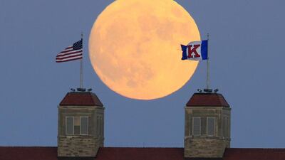 The moon rises beyond flags atop Fraser Hall on the University of Kansas campus in Lawrence, Kansas. Orlin Wagner / AP Photo