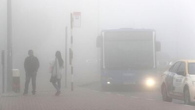 People waiting for the bus during the fog at the bus stop in Discovery Gardens. Pawan Singh / The National.