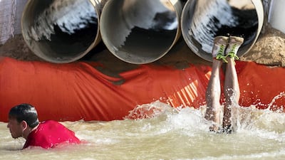 A racer dives into a muddy pool after crawling through a pipe.