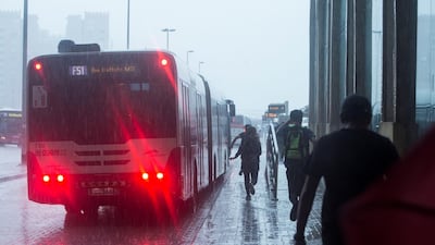 Travellers run for the bus in a bid to escape the wet weather. Leslie Pableo / The National