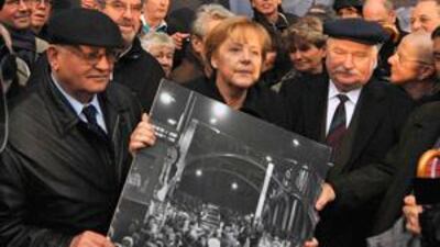 From left, Mikhail Gorbachev, Angela Merkel and Lech Walesa hold a black and white picture showing cars and people at the border crossing after the fall of the Berlin Wall 1989.