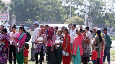 People stand in a queue for food at the Tundikhel relief camp in Kathmandu, a long hit away from the boys' cricket game at mid-on. Pawan Singh / The National