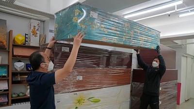 Mr Tong and an employee move a blue floral coffin on top of other paper coffins at the factory in Hong Kong.