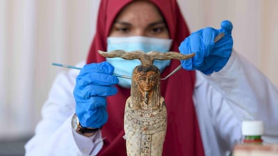 An archaeologist cleans a statue during the unveiling of an ancient treasure trove of more than a 100 intact sarcophagi. AFP