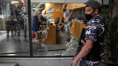 A Lebanese policeman stands guard next to a bank window broken by depositors who had demanded access to their money. An activist group said it will continue to organise bank raids to help people retrieve their trapped savings. AP photo