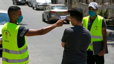 A Palestinian volunteer checks the temperature of a man entering the Amari refugee camp near the West Bank city of Ramallah on July 24, 2020. AFP