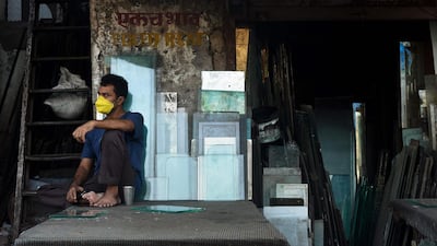 A labourer wearing a face mask sits outside a glass shop in the Dharavi slum. AFP
