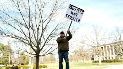 Bernie Trautmann holds a sign in protest of the Michigan State University Board of Trustees while it met on January 26, outside the Hannah Administration Building on the MSU campus in East Lansing. The university's athletic director announced his retirement Friday. Nick King / AP