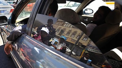 The reflection of three girls from the Hajiri family selling tissues to passing drivers at an intersection in downtown Sanaa.