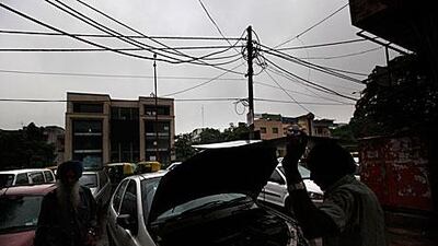 A mechanic repairs a car next to an electric pole which has illegal subsidiary wires attached to the main cables in New Delhi, India, during the power cut yesterday.