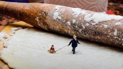 A man pulls a child on a sledge through a snow scene created by flour and pastry. The image is captioned as "In a Cheesecake Factory". Courtesy Omar Maree Humaid