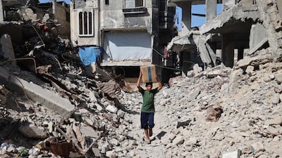A displaced Palestinian boy carries a box of emergency supplies provided by the World Food Programme from an aid distribution point in the ruins of Nuseirat, central Gaza. AFP