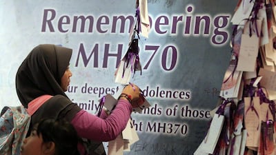 A woman ties a message card for passengers aboard the missing Malaysia Airlines flight MH370, at a shopping mall in Kuala Lumpur. Lai Seng Sin / AP Photo April 5