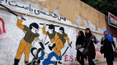 Girls walk past a mural inspired by a widely circulated photo of Egyptian police beating and stripping a veiled female protester, on a recently whitewashed wall with Arabic that reads 'we will not forget you our lady,' in Tahrir Square.