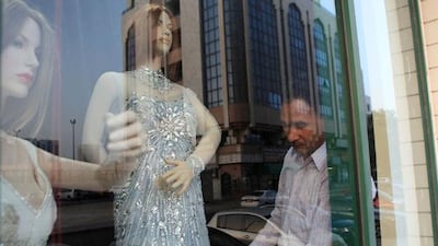 A man fixes a bridal dress on a mannequin in a shop showroom.