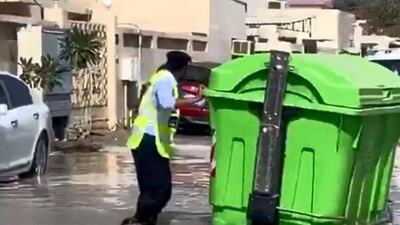 A police officer wades through flood water as he tries to clear a rubbish bin from the middle of a residential road in Kalba on Sharjah's east coast. Courtesy: Sharjah Police