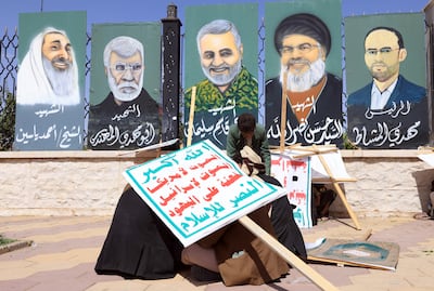 Houthi supporters take shelter from the sun with an anti-US and Israel placard beneath paintings of pro-Iran militant figures in Sanaa. EPA