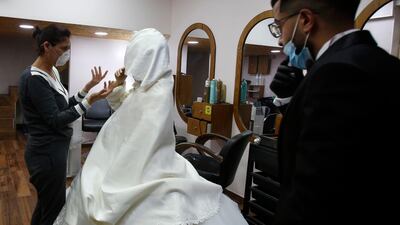 Palestinian groom Imad Sharaf wears gloves and a face mask while a hair dresser puts the finishing touches on his bride Bara'a Amarneh. AFP