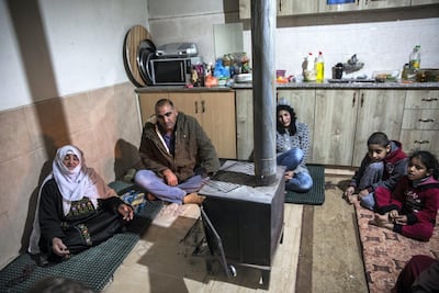 Jaber Abu Queder, 51, head of local council of the unrecognised village of Al Zarnoug with his family as they sit on their kitchen floor around a wood stove to keep warm in the early evening. Heidi Levine for The National.