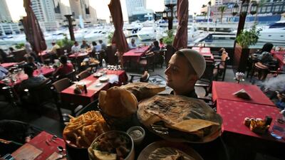 A waiter carries a tray of Arabic food at a restaurant in Dubai Marina. The emirate is now home to more than 16,000 food outlets Kamran Jebreili / AP Photo